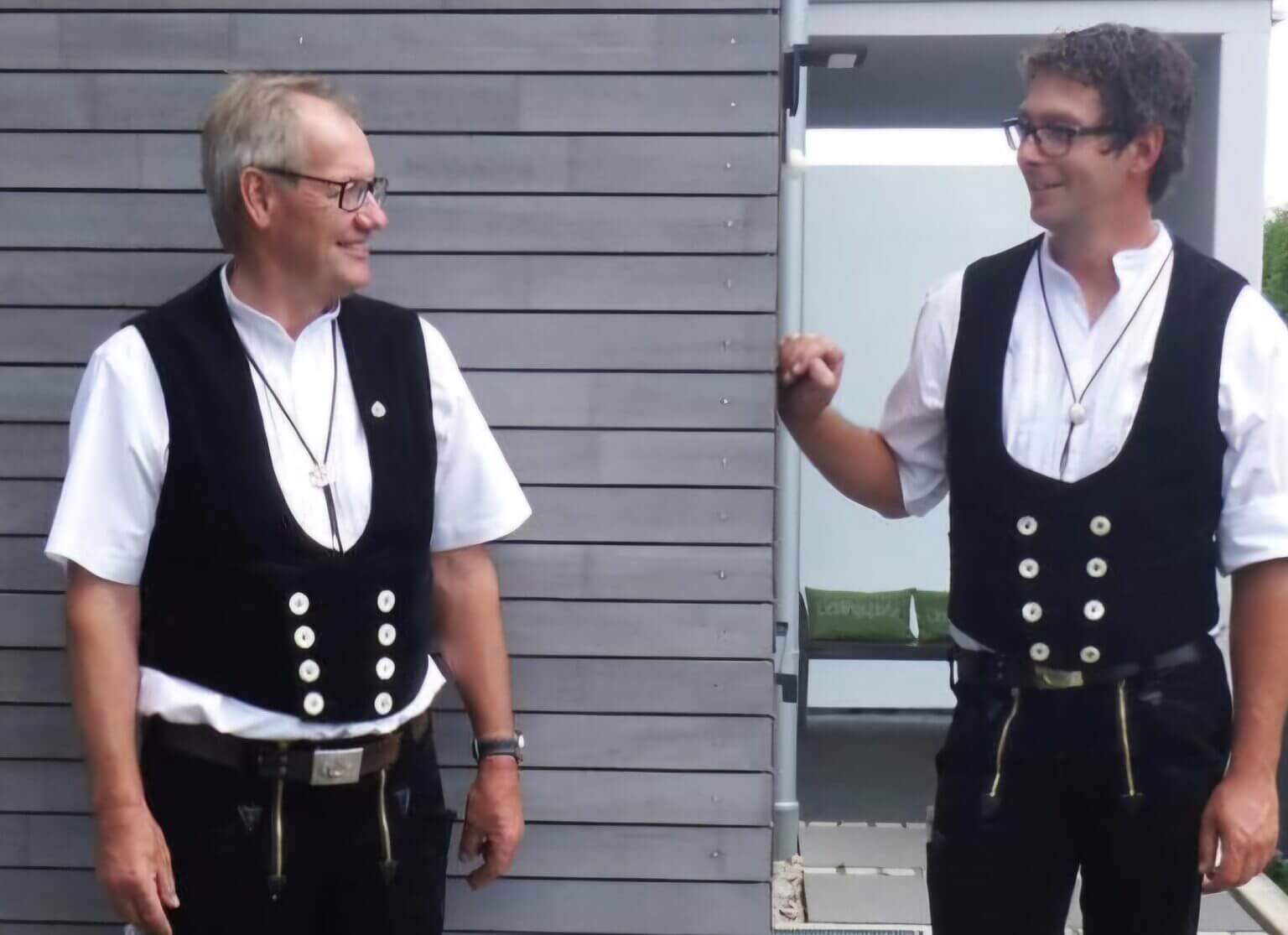 Zwei Handwerker in traditioneller Arbeitskleidung vor einem Gebäude